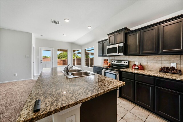 kitchen featuring stainless steel appliances, an island with sink, light colored carpet, lofted ceiling, and decorative backsplash