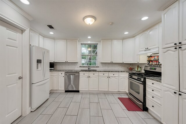 kitchen with sink, white cabinets, backsplash, dark stone counters, and appliances with stainless steel finishes