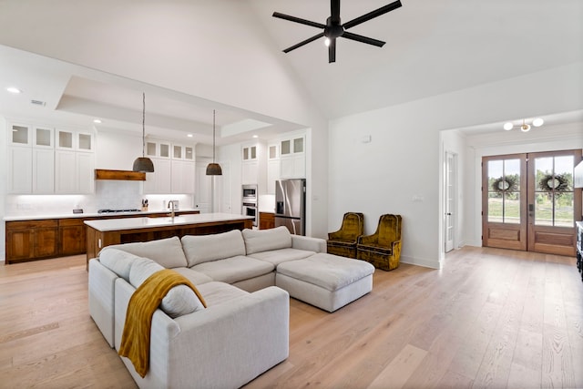 living room featuring light wood-type flooring, sink, a raised ceiling, a high ceiling, and ceiling fan