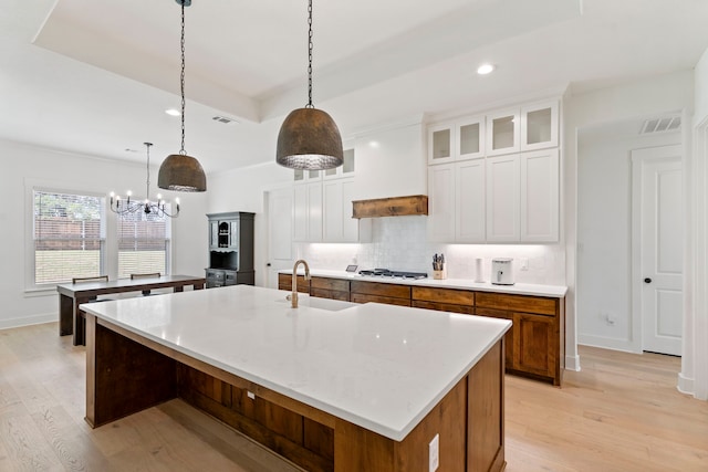 kitchen with decorative light fixtures, white cabinets, a large island with sink, and sink