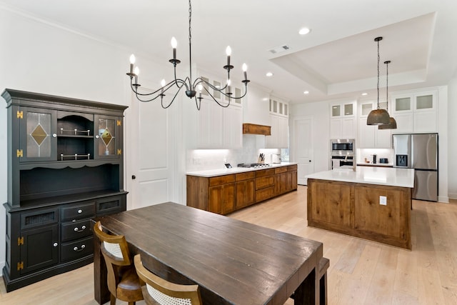 kitchen featuring white cabinetry, light hardwood / wood-style flooring, stainless steel appliances, an island with sink, and a raised ceiling