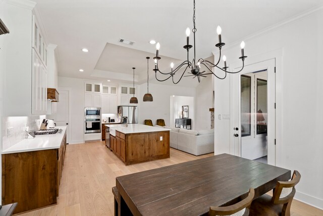 kitchen with pendant lighting, appliances with stainless steel finishes, a center island with sink, white cabinets, and light hardwood / wood-style floors