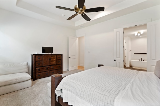 bedroom featuring connected bathroom, light carpet, a tray ceiling, and ceiling fan