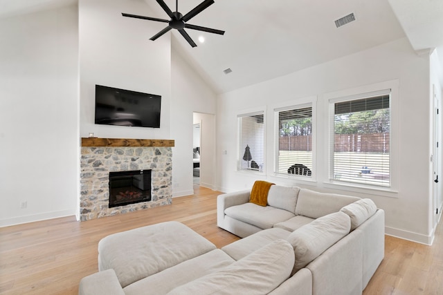 living room with high vaulted ceiling, light hardwood / wood-style flooring, ceiling fan, and a stone fireplace