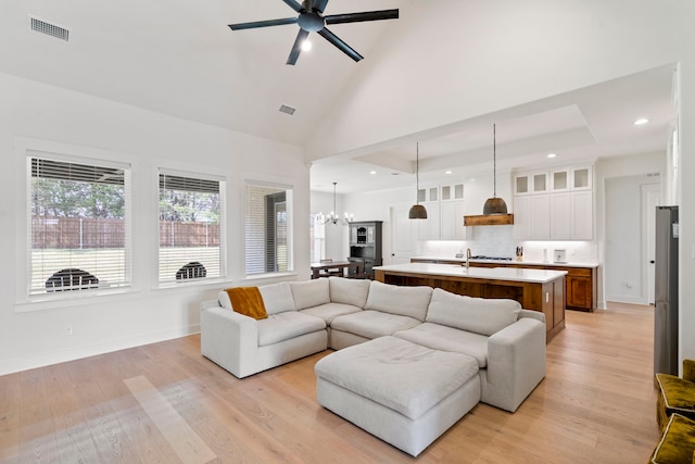 living room featuring ceiling fan with notable chandelier, high vaulted ceiling, and light hardwood / wood-style flooring