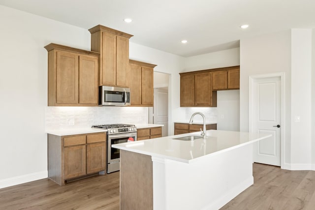 kitchen with decorative backsplash, stainless steel appliances, sink, a center island with sink, and light hardwood / wood-style floors