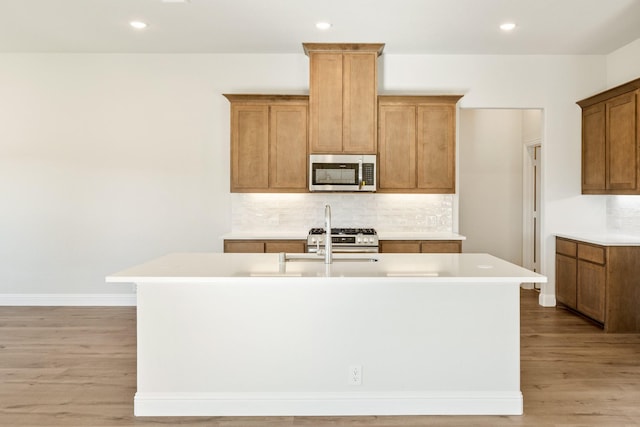 kitchen featuring light wood-type flooring, stainless steel appliances, a center island with sink, and backsplash