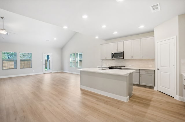 kitchen with a kitchen island with sink, light wood-type flooring, sink, decorative backsplash, and appliances with stainless steel finishes