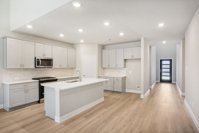 kitchen featuring an island with sink, sink, backsplash, appliances with stainless steel finishes, and light hardwood / wood-style floors