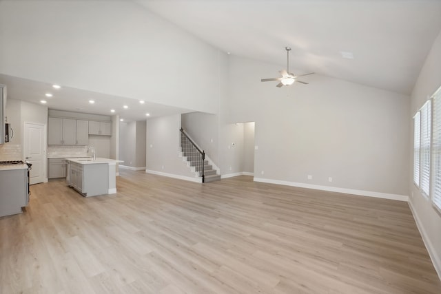 unfurnished living room with high vaulted ceiling, sink, light wood-type flooring, and ceiling fan