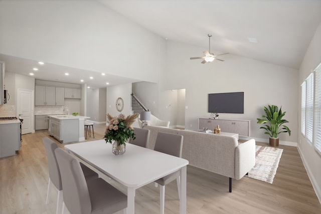 dining space featuring ceiling fan, light wood-type flooring, sink, and high vaulted ceiling