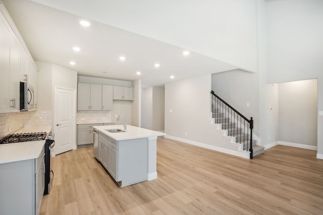 kitchen with light hardwood / wood-style flooring, a center island with sink, sink, backsplash, and appliances with stainless steel finishes