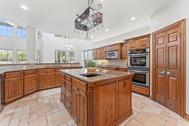 kitchen featuring sink, tasteful backsplash, decorative light fixtures, a center island with sink, and appliances with stainless steel finishes