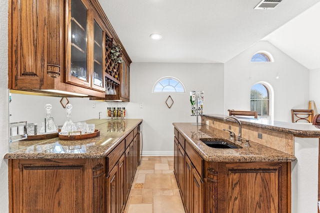 kitchen with lofted ceiling, sink, an island with sink, and stone countertops