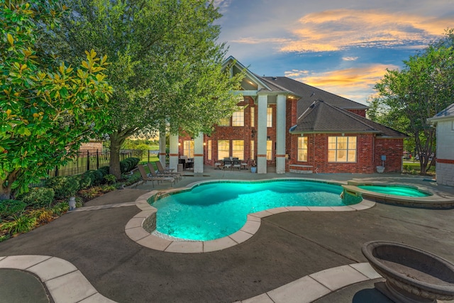 pool at dusk with a patio and an in ground hot tub