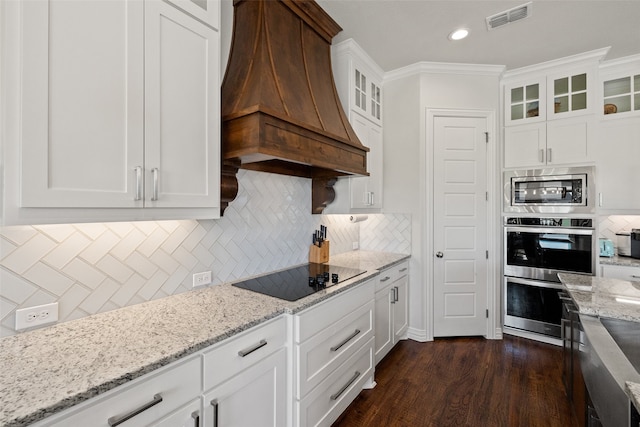 kitchen with custom exhaust hood, crown molding, white cabinetry, decorative backsplash, and appliances with stainless steel finishes