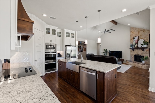 kitchen with vaulted ceiling, stainless steel appliances, sink, a stone fireplace, and ceiling fan