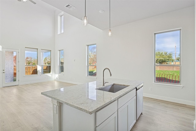 kitchen with sink, light hardwood / wood-style floors, light stone countertops, an island with sink, and decorative light fixtures