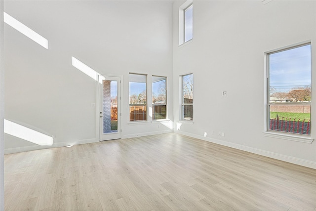 unfurnished living room featuring a high ceiling, plenty of natural light, and light wood-type flooring