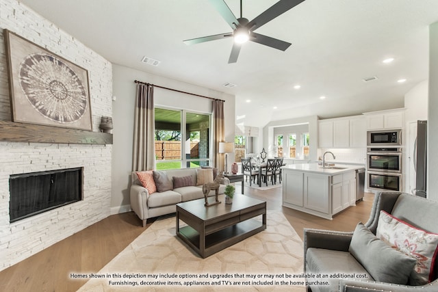 living room with light wood-type flooring, ceiling fan, sink, and a stone fireplace