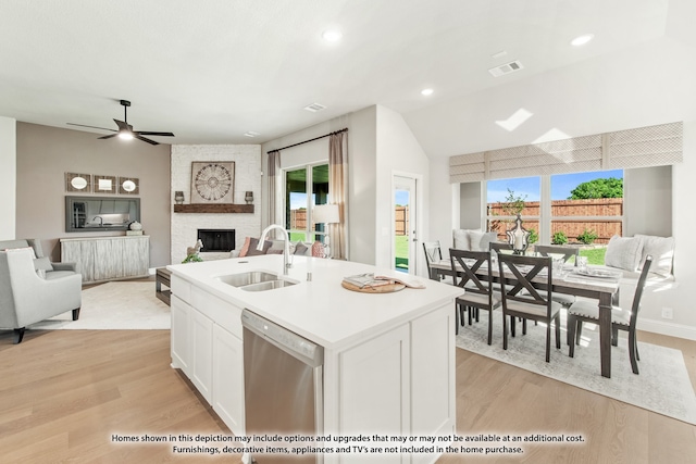 kitchen with sink, stainless steel dishwasher, a center island with sink, white cabinetry, and a fireplace