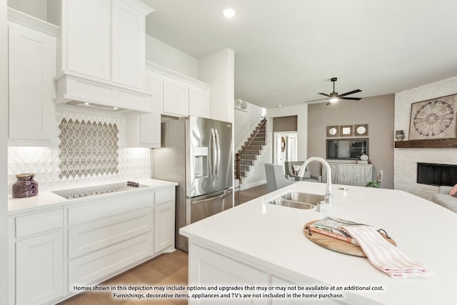 kitchen with ceiling fan, a stone fireplace, white cabinets, and sink