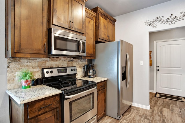 kitchen featuring decorative backsplash, light stone counters, light wood-type flooring, and appliances with stainless steel finishes