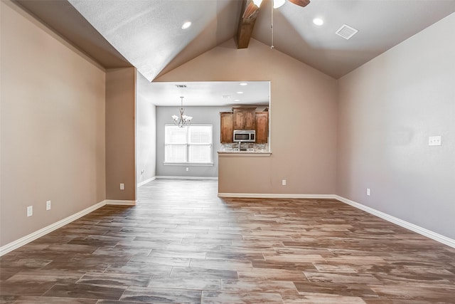 unfurnished living room featuring wood-type flooring, ceiling fan with notable chandelier, and lofted ceiling with beams