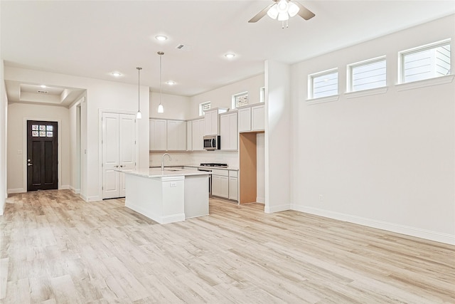 kitchen featuring stainless steel appliances, a kitchen island with sink, sink, light hardwood / wood-style flooring, and hanging light fixtures