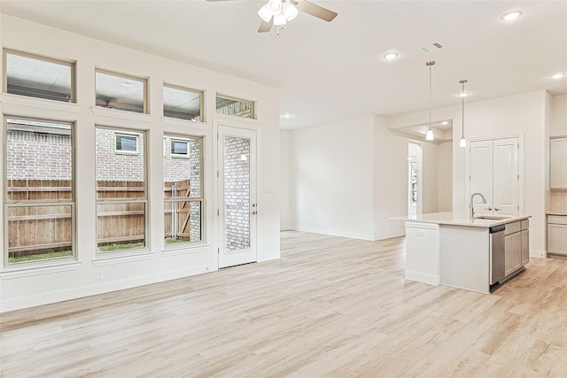 interior space with dishwasher, sink, light hardwood / wood-style flooring, pendant lighting, and a center island with sink