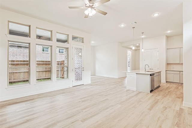 kitchen with dishwasher, a center island with sink, sink, light wood-type flooring, and decorative light fixtures