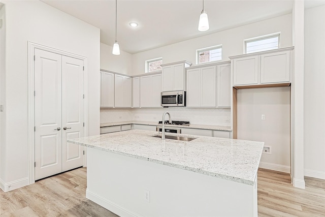 kitchen with pendant lighting, a kitchen island with sink, white cabinets, sink, and light stone countertops