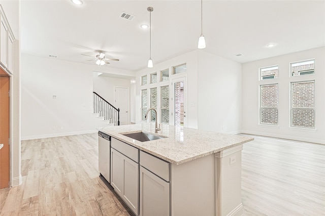 kitchen with light stone countertops, dishwasher, sink, light hardwood / wood-style floors, and a center island with sink