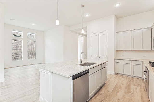 kitchen with a center island with sink, sink, light stone countertops, decorative light fixtures, and stainless steel appliances