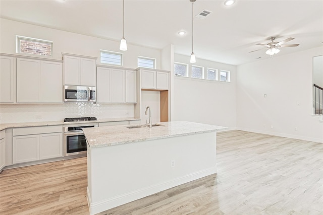 kitchen with sink, hanging light fixtures, light stone counters, a kitchen island with sink, and appliances with stainless steel finishes