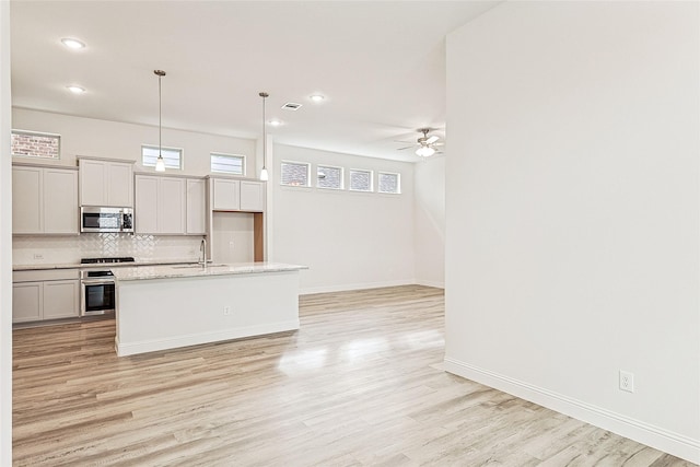 kitchen featuring sink, hanging light fixtures, decorative backsplash, a center island with sink, and appliances with stainless steel finishes