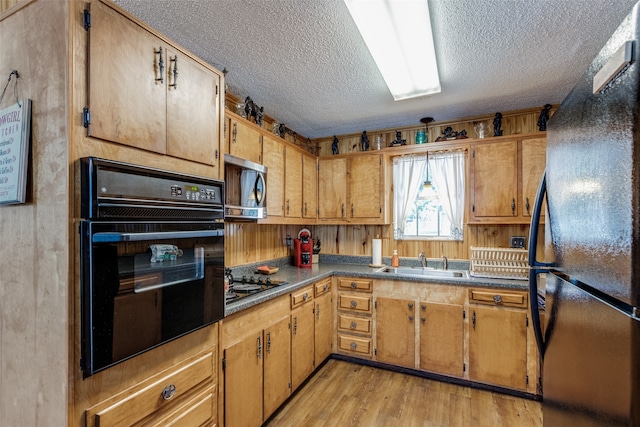 kitchen featuring a textured ceiling, black appliances, sink, and light wood-type flooring