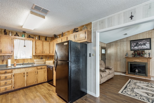 kitchen featuring a textured ceiling, black appliances, light hardwood / wood-style floors, sink, and wooden walls