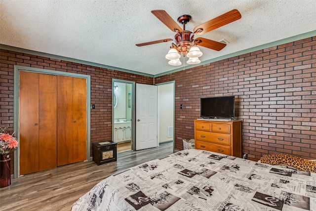 bedroom featuring a closet, ceiling fan, hardwood / wood-style floors, and brick wall