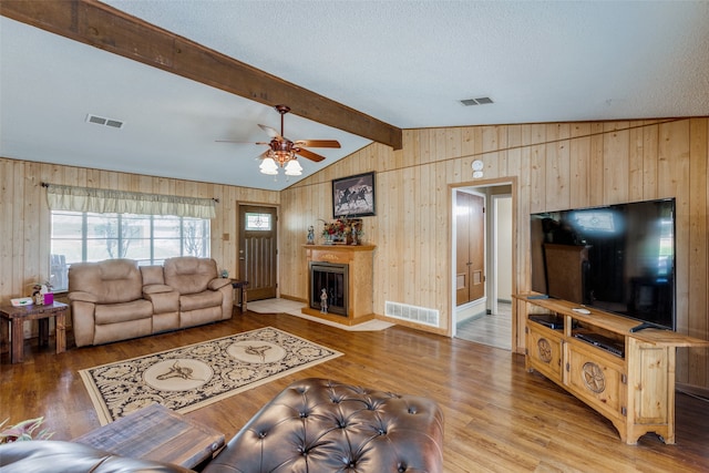 living room with hardwood / wood-style floors, wooden walls, a textured ceiling, ceiling fan, and vaulted ceiling with beams