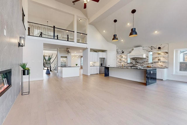 living room featuring ceiling fan, high vaulted ceiling, light hardwood / wood-style flooring, a fireplace, and sink