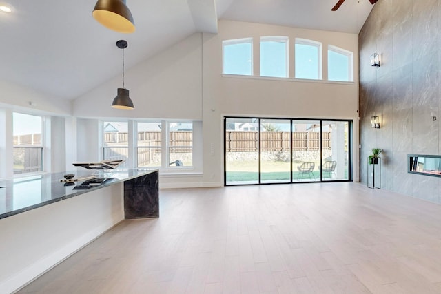 unfurnished living room with light hardwood / wood-style floors, a healthy amount of sunlight, high vaulted ceiling, and a tiled fireplace