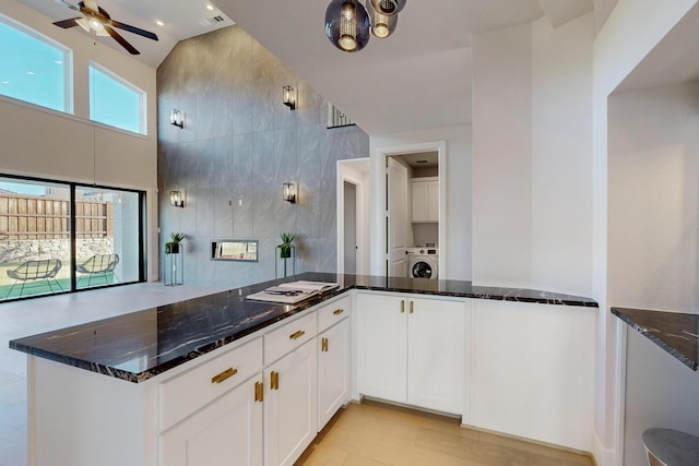 kitchen featuring lofted ceiling, washer / dryer, dark stone countertops, tile walls, and white cabinetry