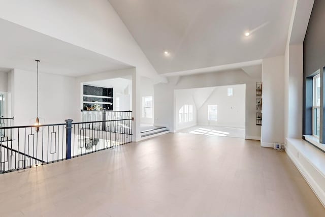 empty room with high vaulted ceiling, a chandelier, and light wood-type flooring