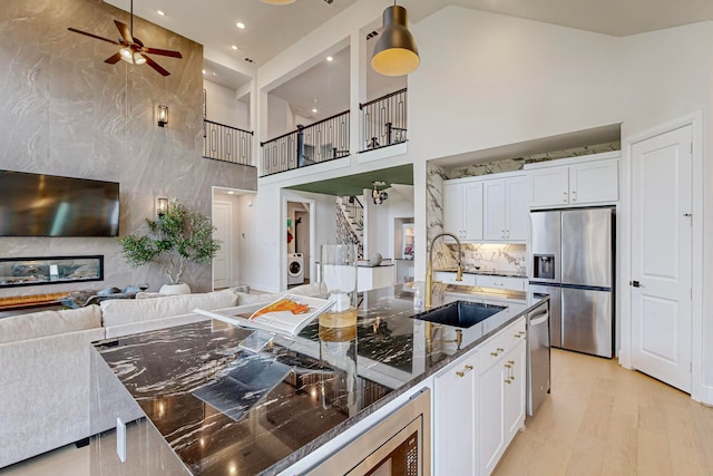 kitchen featuring white cabinets, appliances with stainless steel finishes, high vaulted ceiling, light hardwood / wood-style floors, and sink