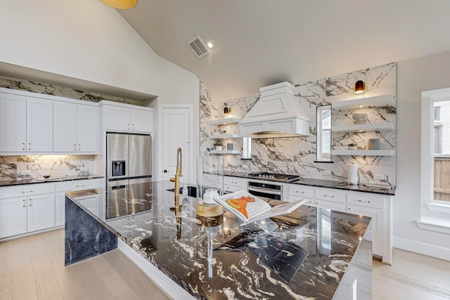 kitchen with tasteful backsplash, light wood-type flooring, stainless steel appliances, white cabinets, and premium range hood