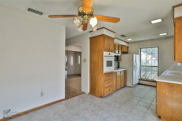 kitchen featuring ceiling fan, white appliances, sink, light tile patterned floors, and a textured ceiling