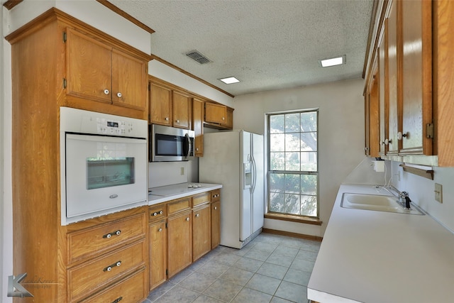 kitchen with light tile patterned floors, sink, white appliances, a textured ceiling, and crown molding