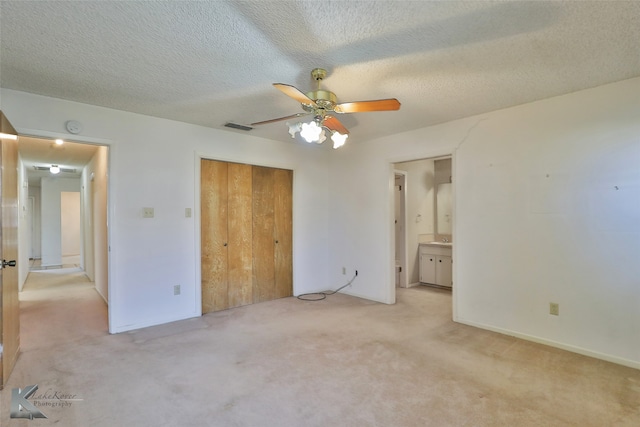 unfurnished bedroom with ceiling fan, a closet, light carpet, connected bathroom, and a textured ceiling