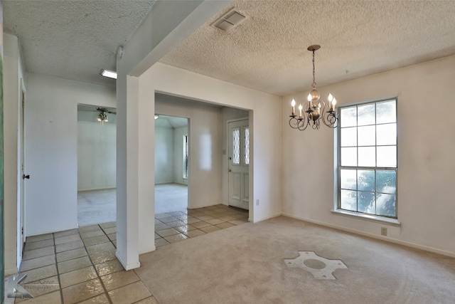 empty room with light carpet, a notable chandelier, and a textured ceiling